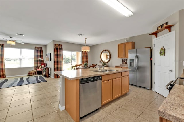 kitchen with appliances with stainless steel finishes, pendant lighting, sink, light tile patterned floors, and a center island with sink