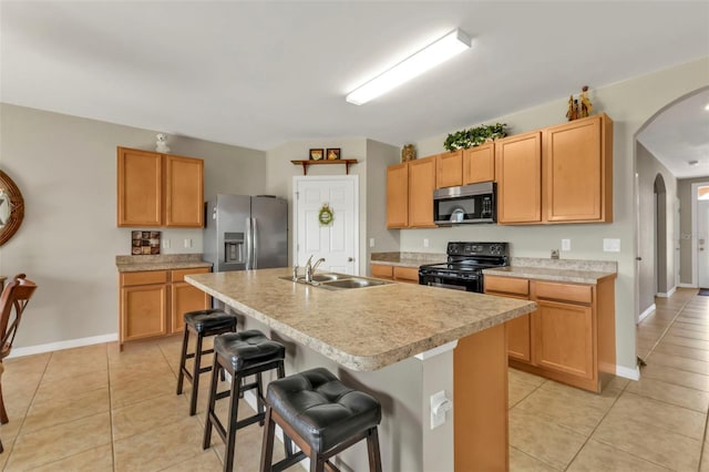 kitchen featuring appliances with stainless steel finishes, a kitchen island with sink, light tile patterned floors, and a kitchen breakfast bar