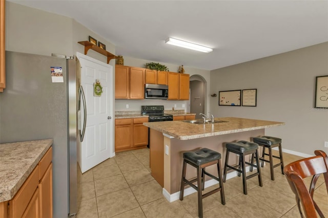 kitchen with light tile patterned flooring, appliances with stainless steel finishes, sink, a kitchen bar, and a center island with sink