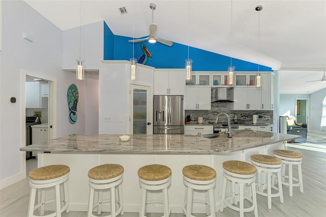 kitchen with pendant lighting, white cabinets, light stone counters, stainless steel fridge with ice dispenser, and wall chimney exhaust hood