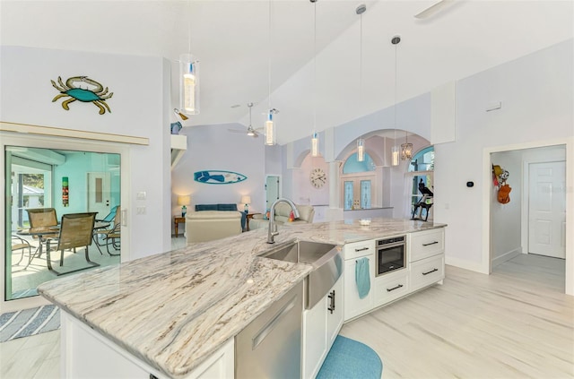 kitchen with arched walkways, white cabinets, open floor plan, decorative light fixtures, and a sink