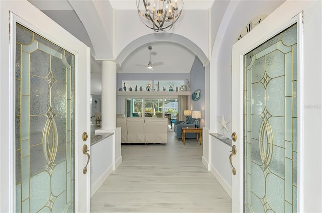 entrance foyer with arched walkways, light wood-style floors, vaulted ceiling, baseboards, and ceiling fan with notable chandelier