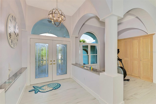 foyer with a notable chandelier, wood finished floors, a towering ceiling, baseboards, and french doors