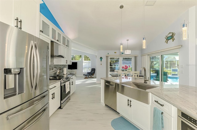 kitchen with wall chimney exhaust hood, sink, white cabinetry, decorative light fixtures, and stainless steel appliances