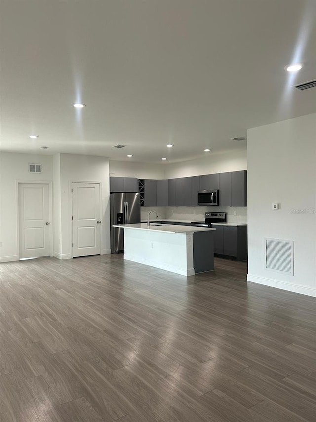 kitchen with wood-type flooring, appliances with stainless steel finishes, sink, and a center island with sink