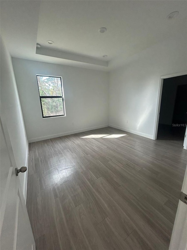 empty room with dark wood-type flooring and a raised ceiling