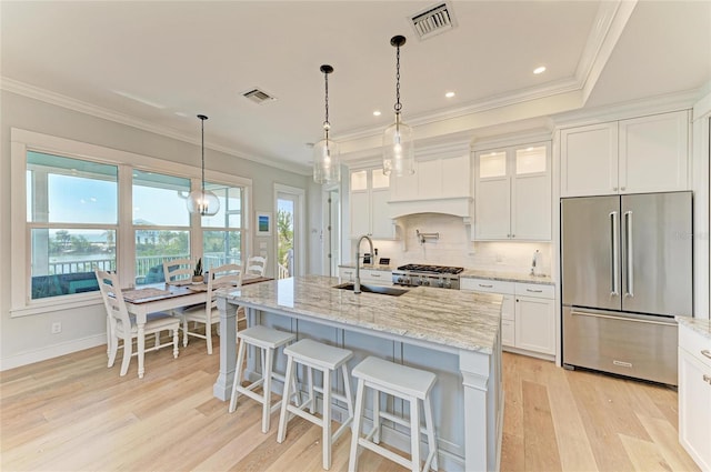 kitchen featuring high end fridge, white cabinetry, light stone countertops, and a center island with sink
