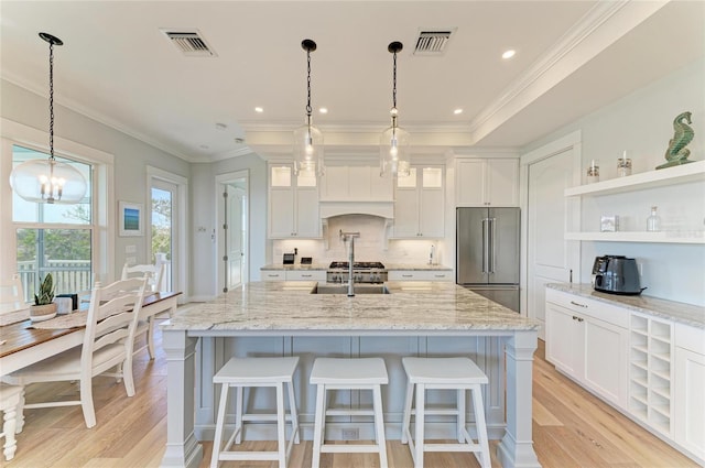 kitchen with pendant lighting, white cabinetry, a kitchen island with sink, light stone counters, and high end fridge
