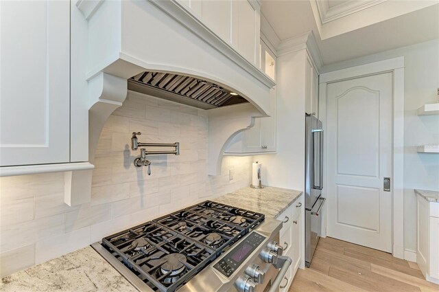 kitchen featuring light hardwood / wood-style flooring, appliances with stainless steel finishes, white cabinetry, backsplash, and light stone counters