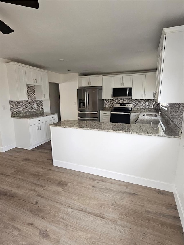 kitchen with white cabinetry, stainless steel appliances, kitchen peninsula, and light stone countertops