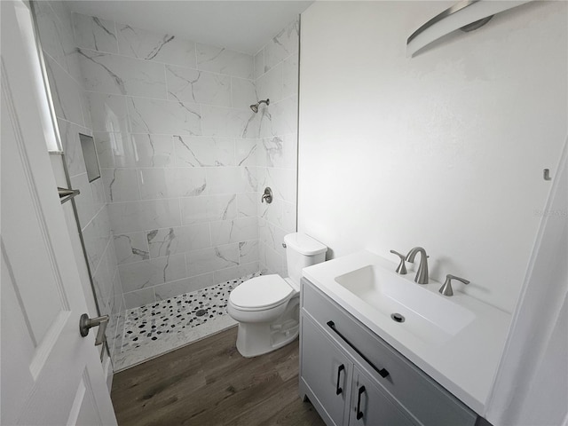 bathroom featuring hardwood / wood-style flooring, vanity, toilet, and a tile shower