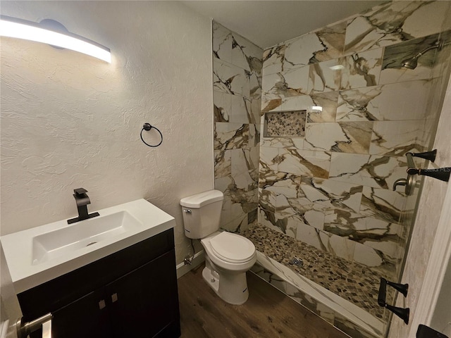 bathroom with a tile shower, hardwood / wood-style floors, vanity, and toilet