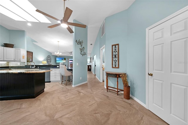 kitchen with pendant lighting, sink, lofted ceiling with skylight, white cabinets, and stainless steel dishwasher