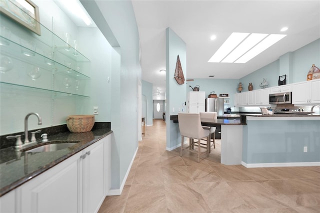 kitchen with sink, white cabinetry, stainless steel appliances, kitchen peninsula, and dark stone counters