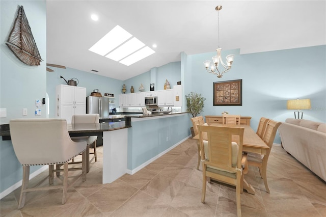 kitchen featuring lofted ceiling with skylight, a breakfast bar, white cabinetry, hanging light fixtures, and stainless steel appliances