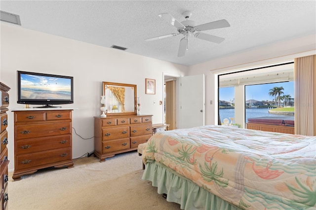 carpeted bedroom with access to exterior, ceiling fan, a textured ceiling, and a water view