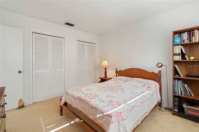 carpeted bedroom with a textured ceiling and multiple closets