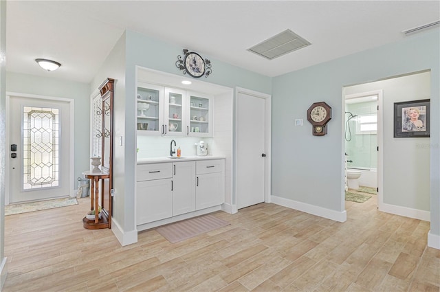 bar featuring tasteful backsplash, white cabinetry, sink, and light hardwood / wood-style floors