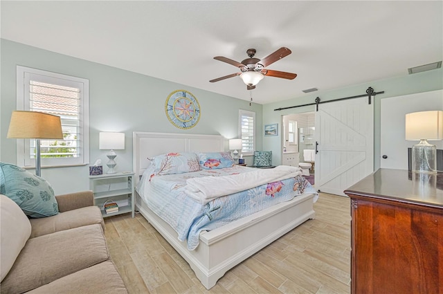 bedroom featuring ceiling fan, ensuite bathroom, a barn door, and light hardwood / wood-style flooring