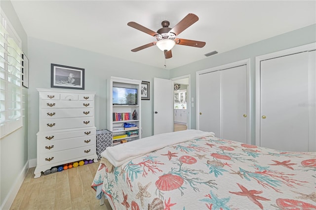 bedroom featuring ceiling fan, light hardwood / wood-style flooring, and two closets