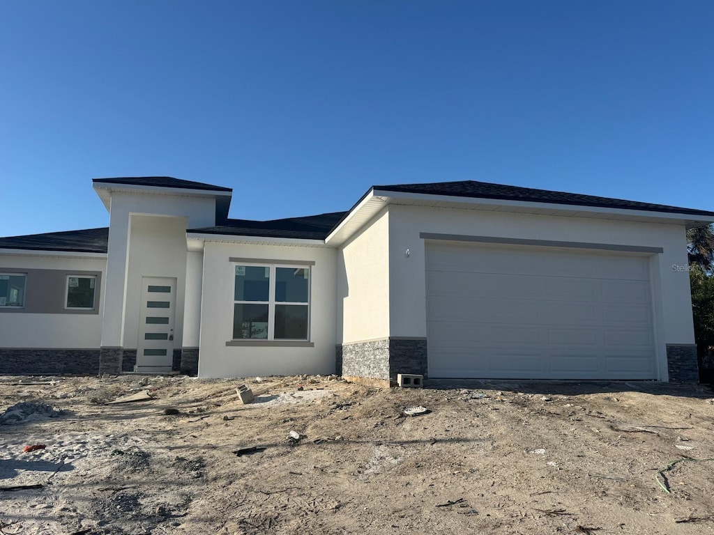 prairie-style house with an attached garage, stone siding, and stucco siding