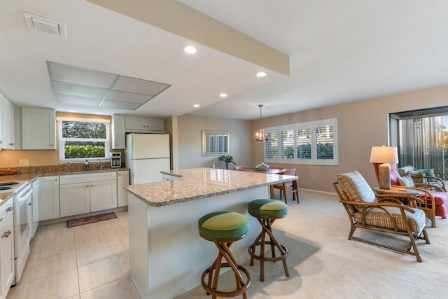 kitchen featuring a kitchen island, a kitchen breakfast bar, hanging light fixtures, light stone countertops, and white appliances