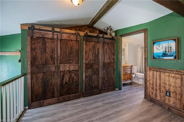 interior space featuring a barn door, lofted ceiling with beams, hardwood / wood-style floors, and wood walls