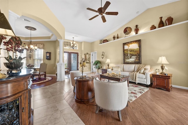 living room featuring lofted ceiling, ornate columns, a tray ceiling, light hardwood / wood-style floors, and ceiling fan with notable chandelier