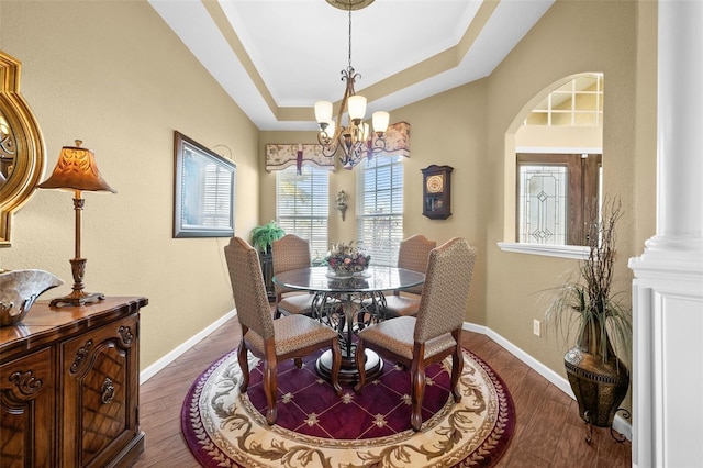 dining room with an inviting chandelier, dark hardwood / wood-style floors, a raised ceiling, and ornate columns