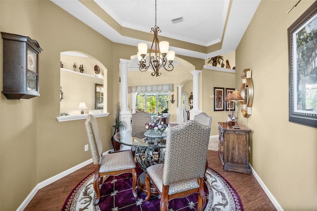 dining room with decorative columns, a raised ceiling, wood-type flooring, and a chandelier