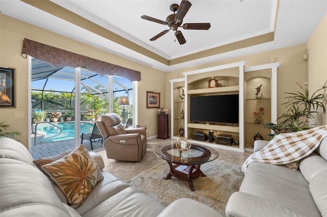 living room featuring crown molding, built in shelves, a raised ceiling, and ceiling fan