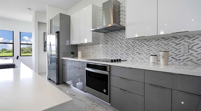 kitchen with appliances with stainless steel finishes, sink, white cabinets, decorative backsplash, and wall chimney exhaust hood