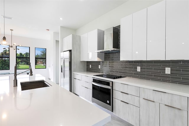 kitchen with wall chimney exhaust hood, sink, decorative light fixtures, appliances with stainless steel finishes, and white cabinets