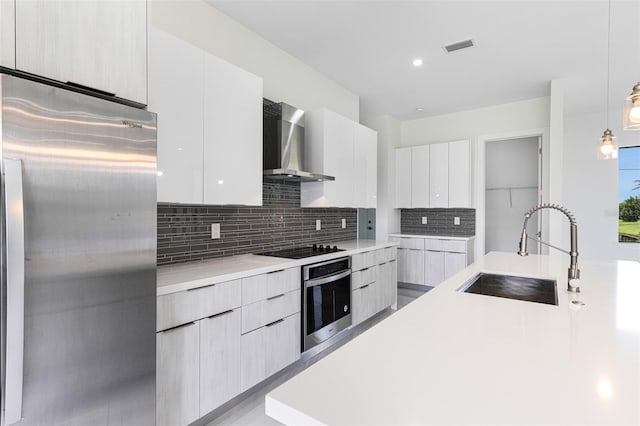 kitchen featuring appliances with stainless steel finishes, pendant lighting, sink, white cabinets, and wall chimney exhaust hood