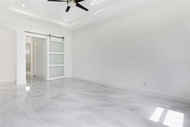 unfurnished bedroom featuring ceiling fan, a tray ceiling, and a barn door