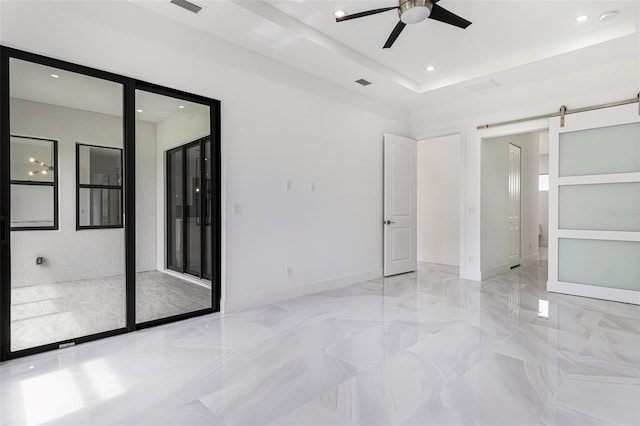 unfurnished bedroom with ceiling fan, a tray ceiling, and a barn door