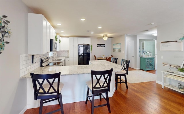 kitchen featuring white cabinetry, a kitchen breakfast bar, hardwood / wood-style flooring, kitchen peninsula, and stainless steel appliances