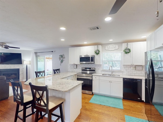 kitchen featuring a kitchen bar, sink, black appliances, ceiling fan, and white cabinets