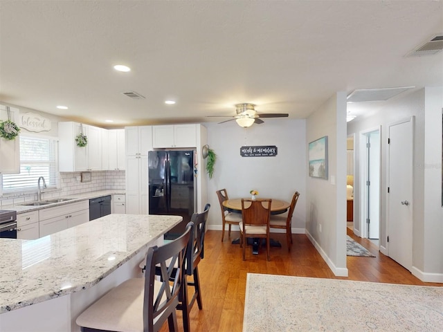 kitchen with white cabinetry, a kitchen breakfast bar, light hardwood / wood-style floors, black appliances, and light stone countertops