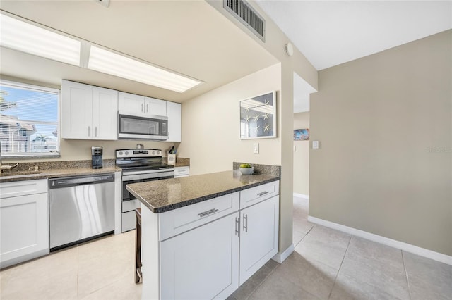 kitchen featuring light tile patterned floors, white cabinetry, stainless steel appliances, a kitchen bar, and dark stone counters