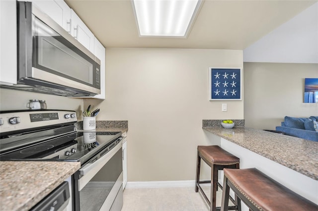 kitchen featuring light tile patterned floors, a breakfast bar, appliances with stainless steel finishes, white cabinetry, and light stone counters