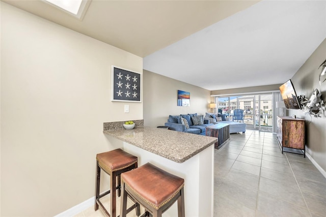 kitchen featuring light tile patterned floors, a skylight, kitchen peninsula, and a kitchen bar