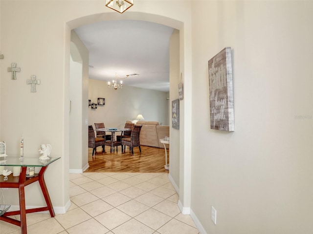 corridor featuring light tile patterned flooring and a notable chandelier