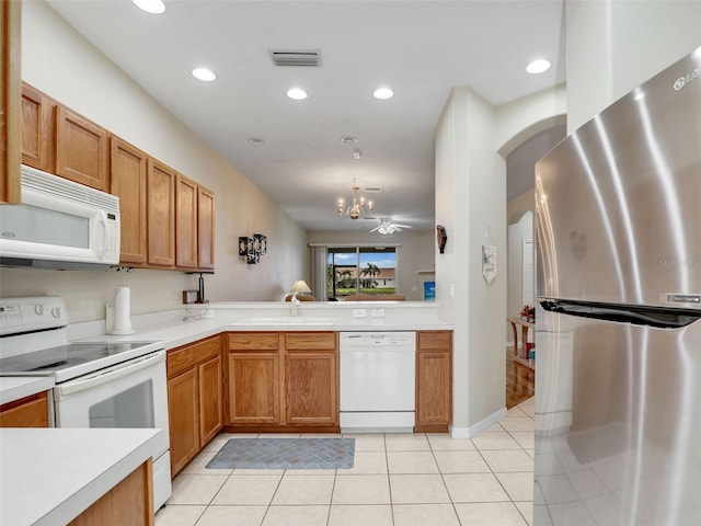 kitchen with light tile patterned flooring, sink, hanging light fixtures, kitchen peninsula, and white appliances