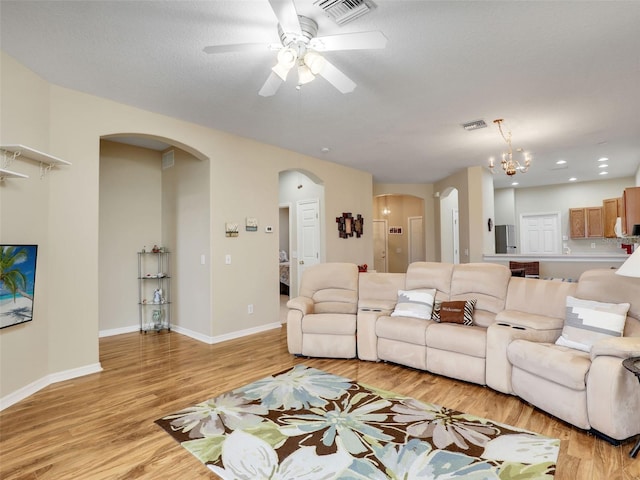 living room with ceiling fan with notable chandelier, light hardwood / wood-style floors, and a textured ceiling