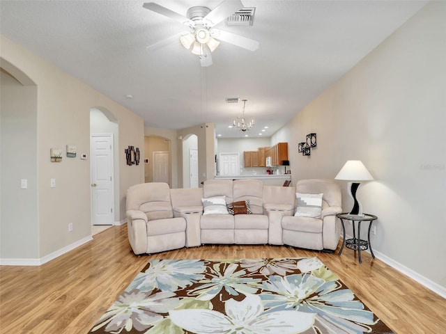 living room featuring ceiling fan with notable chandelier and light hardwood / wood-style flooring