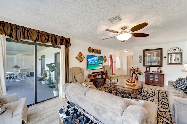 living room with ceiling fan, a textured ceiling, and light wood-type flooring