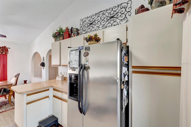 kitchen featuring stainless steel fridge, kitchen peninsula, white cabinets, and light wood-type flooring