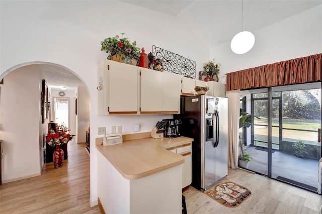 kitchen with white cabinetry, high vaulted ceiling, stainless steel fridge, kitchen peninsula, and pendant lighting