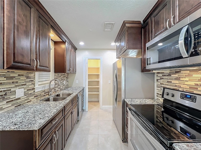 kitchen featuring sink, decorative backsplash, light tile patterned floors, stainless steel appliances, and light stone countertops